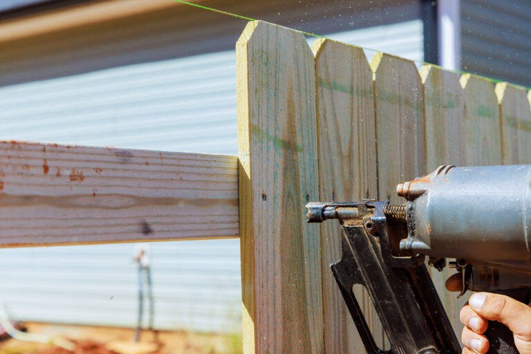 Worker fastening wooden fence boards with a pneumatic nail gun